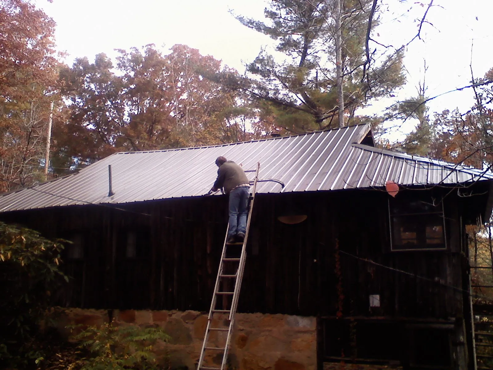 Roofer on a ladder working along the edge of a cabin metal roof in Rockford